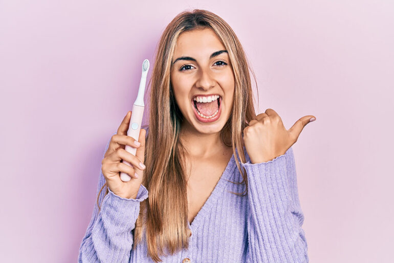 Woman holding electric toothbrush pointing thumb up to the side smiling happy